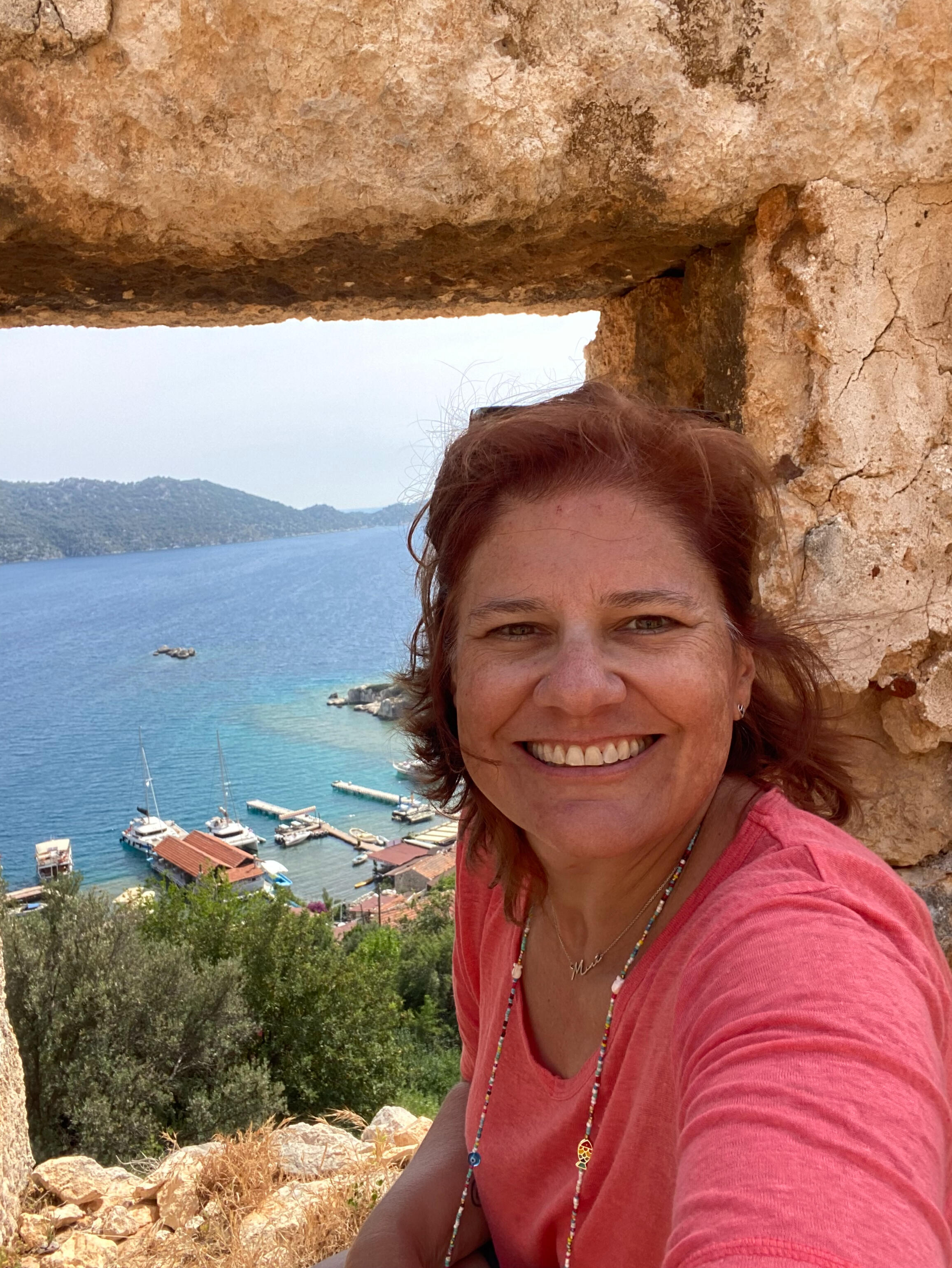 Poet and author Mina Grace framed by ancient stone ruins overlooking a turquoise harbor in Kekova, Türkiye.